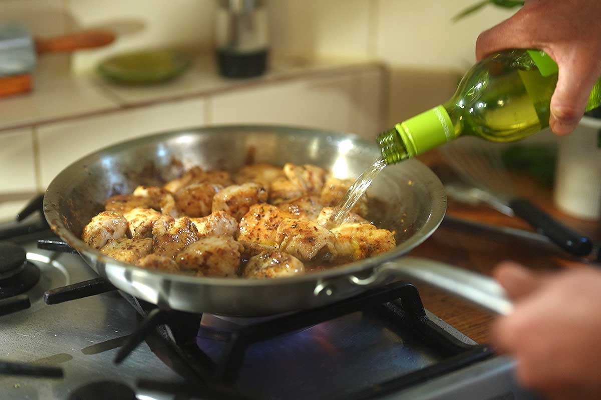 Wine being poured into pan and fond being scraped up from base